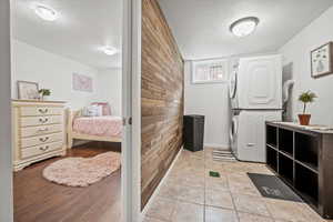 Laundry area featuring stacked washing machine and dryer, a textured ceiling, wooden walls, and baseboards