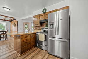 Kitchen with stainless steel appliances, a peninsula, under cabinet range hood, brown cabinets, and light wood-style flooring