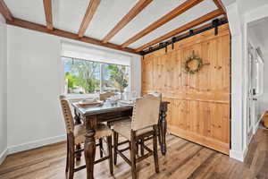 Dining space featuring beamed ceiling, wood finished floors, baseboards, and a barn door