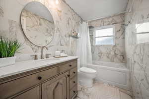 Bathroom featuring tile walls, shower / tub combo with curtain, vanity, toilet, and marble finish flooring