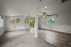 Carpeted spare room featuring a wall unit AC, plenty of natural light, vaulted ceiling, ceiling fan, and baseboards