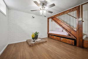 Interior space featuring brick wall, stairs, a ceiling fan, hardwood / wood-style flooring, and baseboards