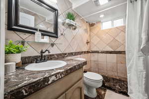 Full bath with tiled shower, toilet, vanity, and marble finish floors
