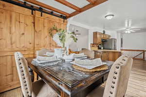 Dining space with light wood-style floors, ceiling fan, and a barn door