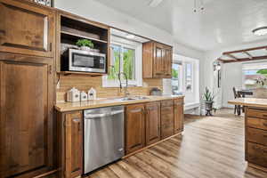Kitchen with stainless steel appliances, a sink, tasteful backsplash, light countertops, and light wood-style flooring