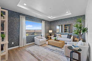 Living area featuring a tray ceiling, wood finished floors, recessed lighting, wallpapered walls, and baseboards