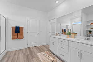 Full bath with wood finished floors, a stall shower, double vanity, recessed lighting, and baseboards
