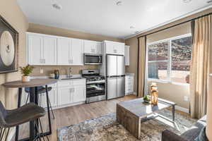 Kitchen with stainless steel appliances, a sink, light wood-type flooring, white cabinets, and baseboards