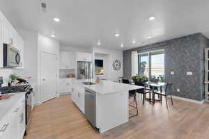 Kitchen featuring stainless steel appliances, a sink, recessed lighting, light wood finished floors, and an island with sink