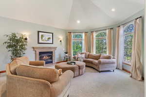 Living room with baseboards, light carpet, a fireplace with flush hearth, vaulted ceiling, and recessed lighting