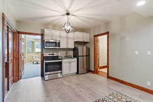 Kitchen featuring stainless steel appliances, baseboards, light wood finished floors, white cabinets, and a sink