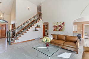Tiled living area with a high ceiling, stairs, arched walkways, baseboards, and a chandelier