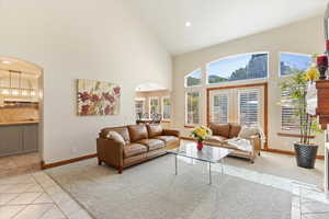 Living room with arched walkways, high vaulted ceiling, light tile patterned flooring, baseboards, and recessed lighting