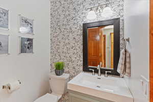 Half bathroom with toilet, wallpapered walls, and vanity