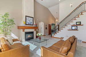 Light carpet living area with arched walkways, stairs, high vaulted ceiling, a large fireplace, and baseboards