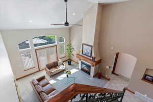 Carpeted living room with high vaulted ceiling, baseboards, a large fireplace, ceiling fan, and recessed lighting