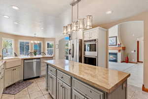 Kitchen featuring appliances with stainless steel finishes, a sink, a chandelier, light tile patterned floors, and a kitchen island