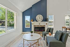 Living area with healthy amount of natural light, wood finished floors, high vaulted ceiling, baseboards, and a fireplace