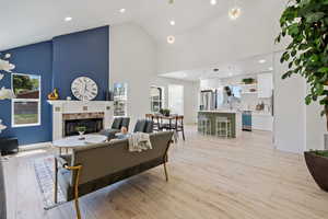 Living area featuring high vaulted ceiling, a tiled fireplace, light wood-style flooring, and recessed lighting