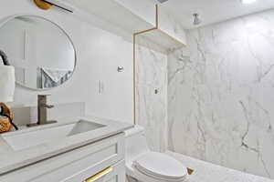 Full bath featuring vanity, a marble finish shower, and toilet