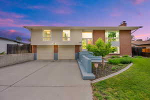 Split foyer home featuring brick siding, an attached garage, a chimney, and driveway