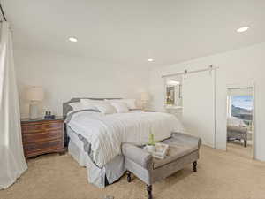 Bedroom with light carpet, a barn door, recessed lighting, and connected bathroom