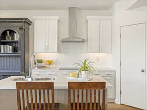 Kitchen featuring wall chimney range hood, a sink, white cabinetry, and light countertops