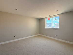 Unfurnished room with light carpet, baseboards, and a textured ceiling