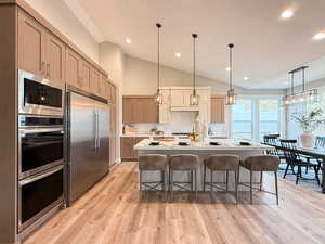 Kitchen with tasteful backsplash, an island with sink, built in appliances, decorative light fixtures, and light brown cabinets