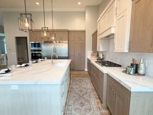 Kitchen featuring light wood-style flooring, built in appliances, light stone counters, decorative light fixtures, and recessed lighting