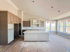 Kitchen featuring a textured ceiling, a kitchen island, vaulted ceiling, open shelves, and light stone counters