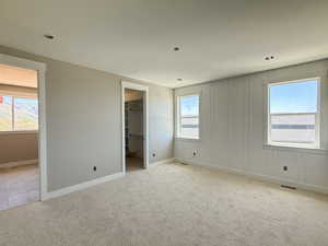 Unfurnished bedroom with light colored carpet, a textured ceiling, a spacious closet, and baseboards