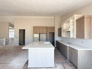 Kitchen featuring a center island, stovetop, a textured ceiling, open shelves, and light stone countertops