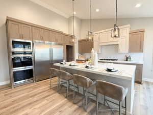 Kitchen with built in appliances, light brown cabinetry, a breakfast bar area, pendant lighting, and decorative backsplash