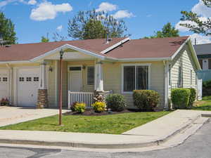 View of front facade with a porch, a garage, concrete driveway, a front lawn, and roof with shingles