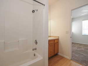Full bath with vanity, washtub / shower combination, wood finished floors, and baseboards