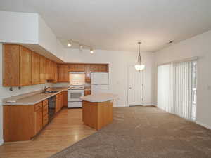 Kitchen with white appliances, a sink, light countertops, a kitchen island, and hanging light fixtures