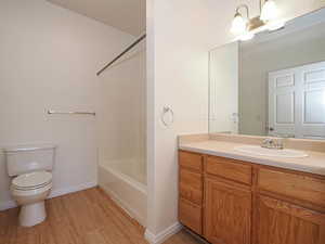 Full bath with wood finished floors, toilet, baseboards, vanity, and bathing tub / shower combination