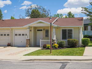 View of front of home with an attached garage, covered porch, a shingled roof, and a front yard
