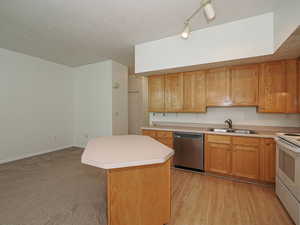 Kitchen featuring stainless steel dishwasher, a sink, electric range, light countertops, and a kitchen island