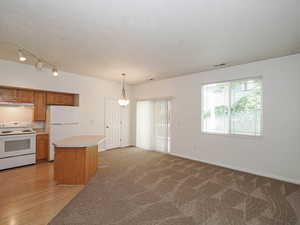 Kitchen featuring white appliances, under cabinet range hood, light countertops, hanging light fixtures, and a center island