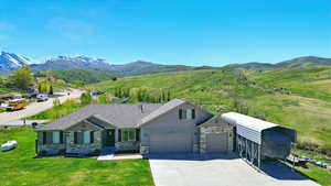 View of front of property with stone siding, a mountain view, driveway, an attached garage, and a front yard