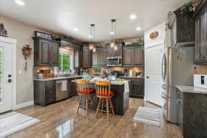 Kitchen with stainless steel appliances, dark brown cabinetry, a kitchen island, decorative backsplash, and a kitchen breakfast bar