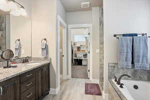 Bathroom featuring a bath, vanity, wood finished floors, baseboards, and tiled shower
