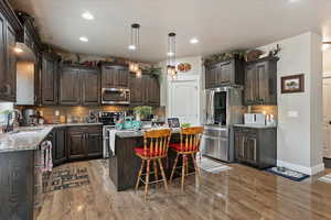 Kitchen with appliances with stainless steel finishes, a sink, dark brown cabinets, a center island, and tasteful backsplash
