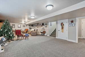 Living area with a textured ceiling, carpet flooring, stairs, and baseboards
