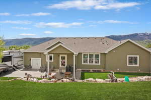 Back of house with a mountain view, stucco siding, a patio, and a lawn