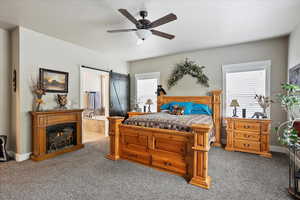 Carpeted bedroom featuring multiple windows, connected bathroom, a barn door, ceiling fan, and a textured ceiling