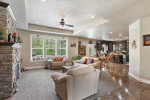 Living area featuring a textured ceiling, baseboards, a ceiling fan, dark wood-type flooring, and a stone fireplace
