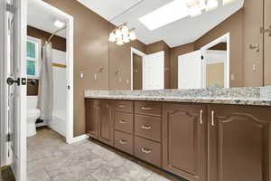 2nd updated full bathroom upstairs featuring toilet, double vanity, shower / tub combo, baseboards, and a skylight
